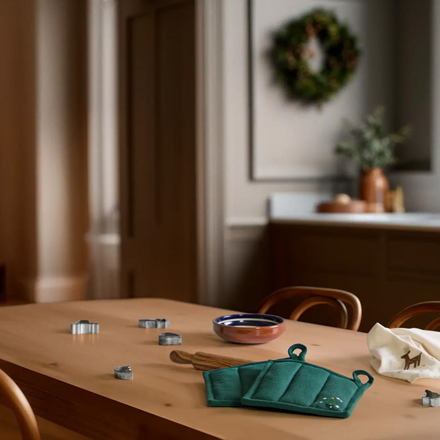 Julegrønn JUNA Christmas Fable gryteklut med brodert juletre på kjøkkenbordet, sammen med annet juleinspirert kjøkkentilbehør.