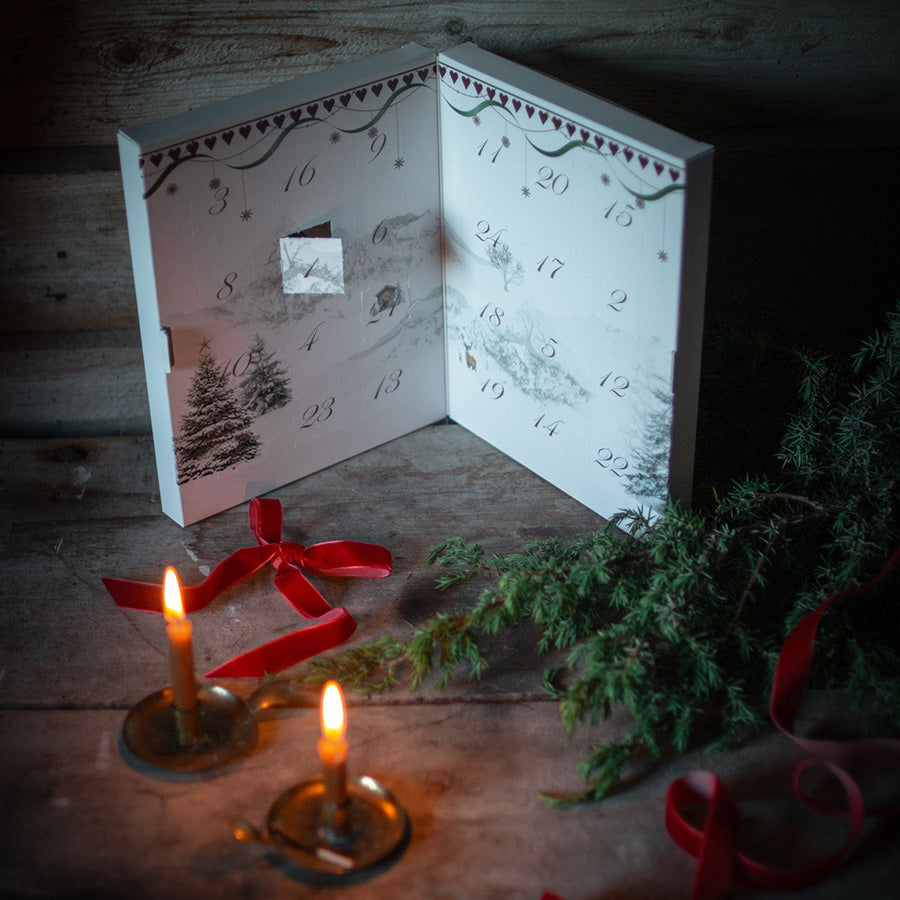 Julemorgen sjokoladekalender åpen med julepynt, levende lys og grankvister