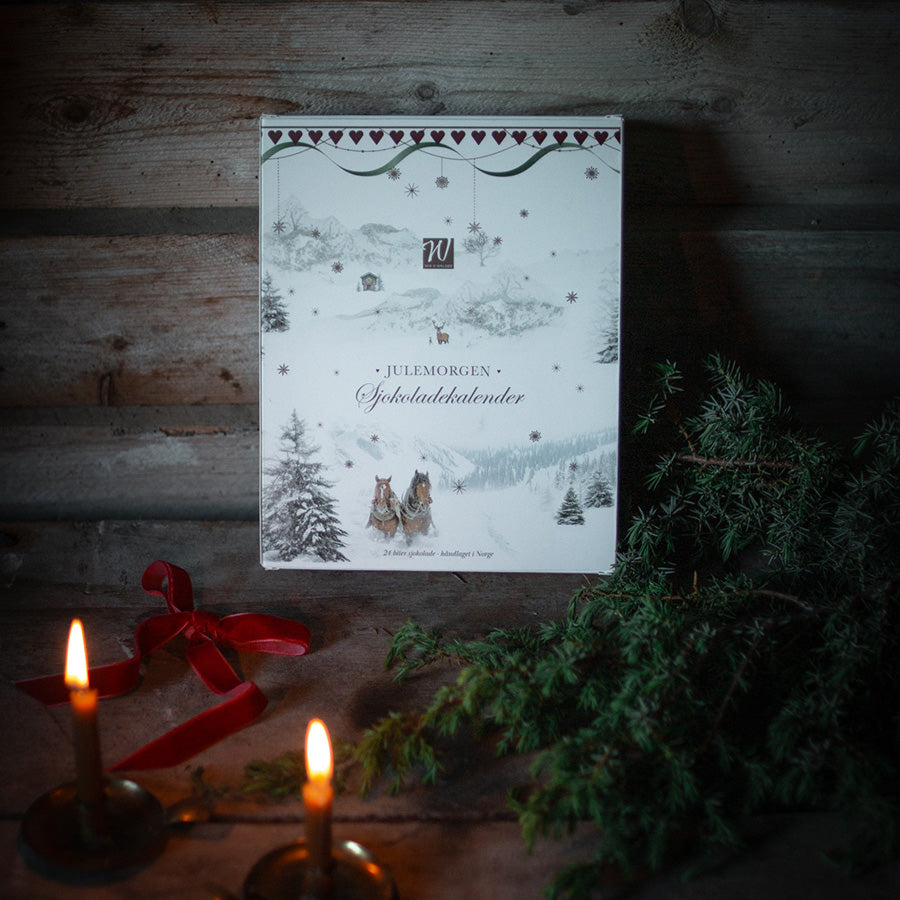 Julemorgen sjokoladekalender med julemotiv, rødt bånd, levende lys og grankvister