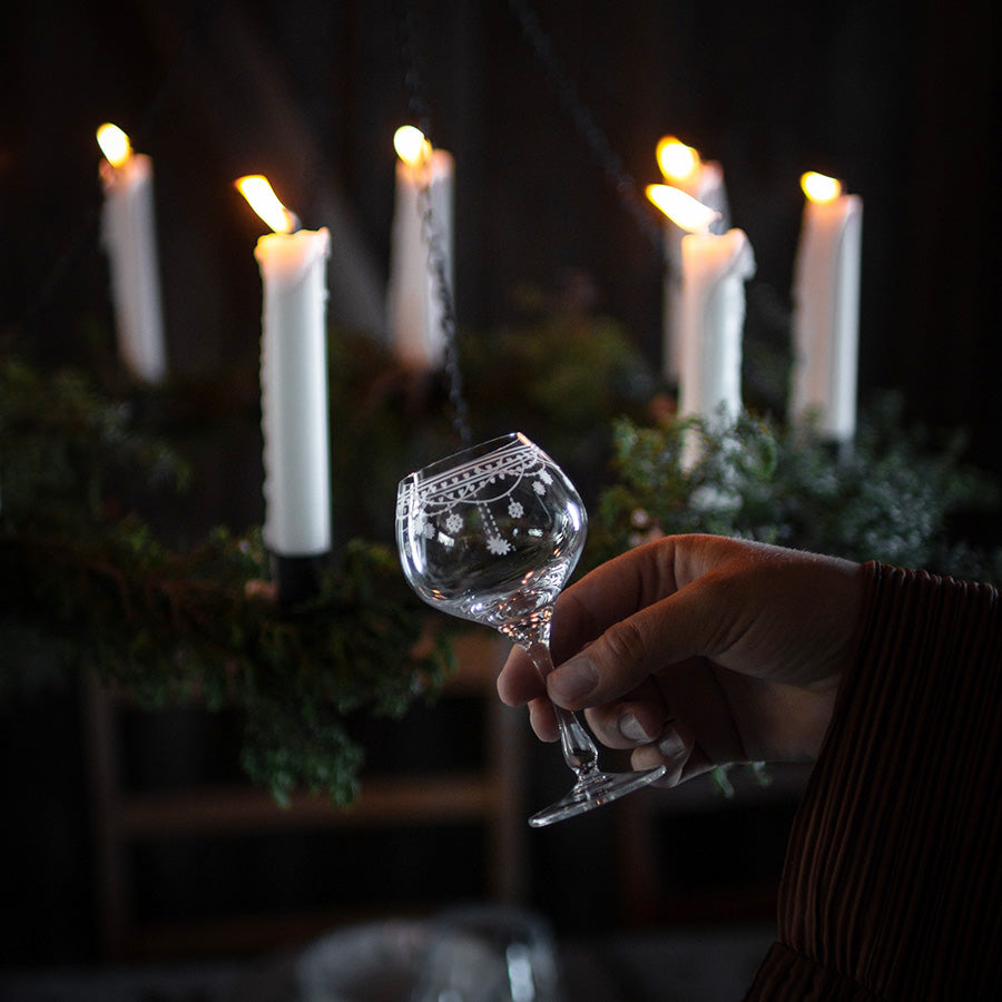 Julemorgen akevittglass fra Wik & Walsøe holdes i hånden foran tente julelys