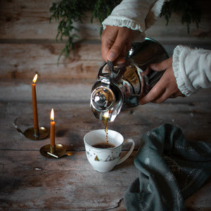 Julemorgen Story kopp fylles med kaffe fra en sølvfarget kaffekanne i stemningsfull julebelysning