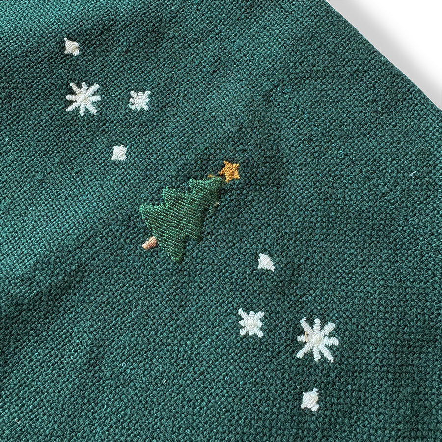 Nærbilde av brodert juletre og hvite julestjerner på grønt JUNA Christmas Fable forkle