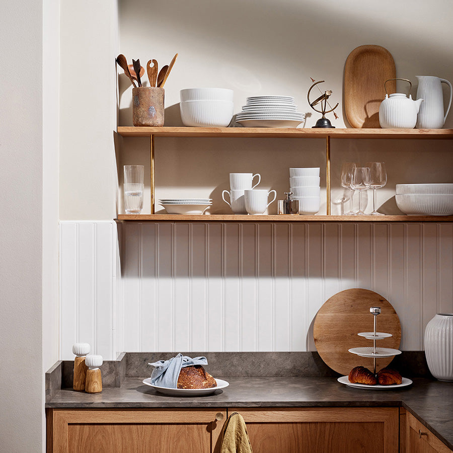 Kähler Hammershøi etasjefat 28 cm i hvit, plassert på en stilfull hylle med keramikk og kjøkkenutstyr, fremhever elegansen av etasjefatet.