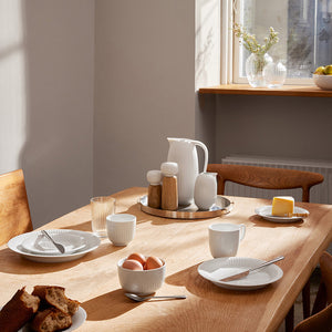 Kähler Hammershøi Mugge 50cl Hvit plassert på et dekket bord med ulike servise, ideell for frokost eller middag.