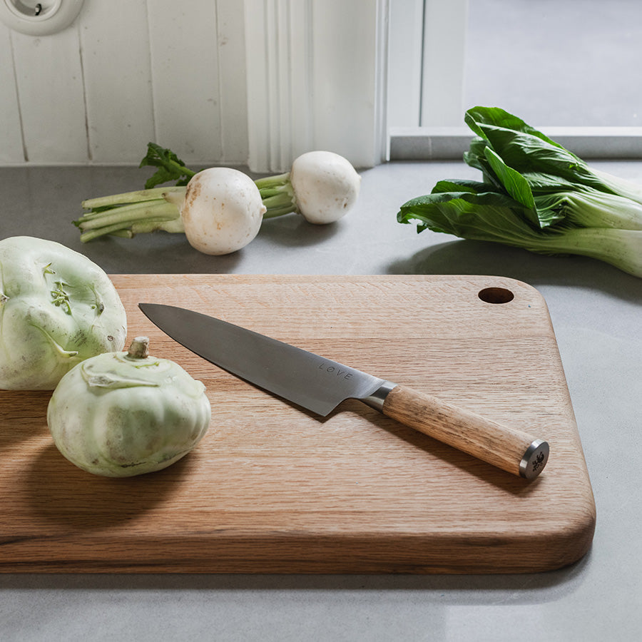 Løve Steig Kokkekniv 20 cm i bruk på en kjøkkenbenk med grønnsaker, viser knivens skarphet og design i naturlige omgivelser.