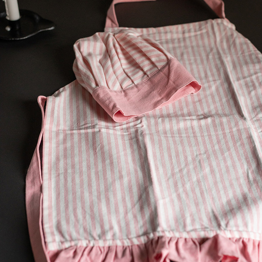 Rosa forkle og kokkehatt i striper, pent plassert sammen, ideelt for unge matlagingsentusiaster.