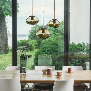 Elegant Hadeland Glassverk Crystal Stone Pendellampe Mooka 3stk over et spisebord, viser tre munnblåste pendellamper i dype kakao-nyanser, plassert i et rom som fremhever naturlig lys og grønn utendørs utsikt.