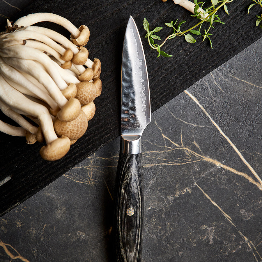 Skrellekniv fra Nordic Blades Legacy Blades 9cm, brukt til skrelling av grønnsaker, sammen med ferske sopp og urter på kjøkkenbenken.