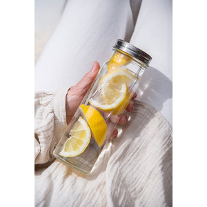 En person holder en Norgesglass flaske med skiver av sitron og iskaldt vann, perfekt for servering og oppbevaring. Flaske i klart glass med metallskrukork, ideell for hverdagsbruk.