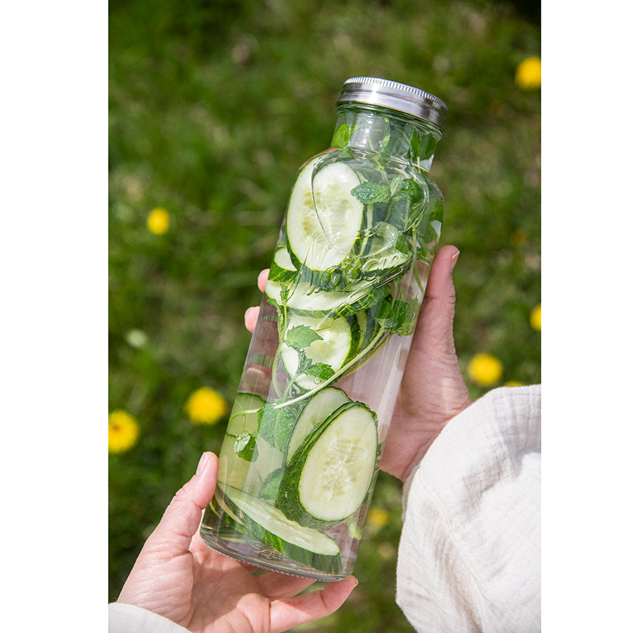 Nærbilde av en Norgesglasset flaske med agurk og mynte, holdt av en person, ideell for helsedrikker og sommerforfriskninger.
