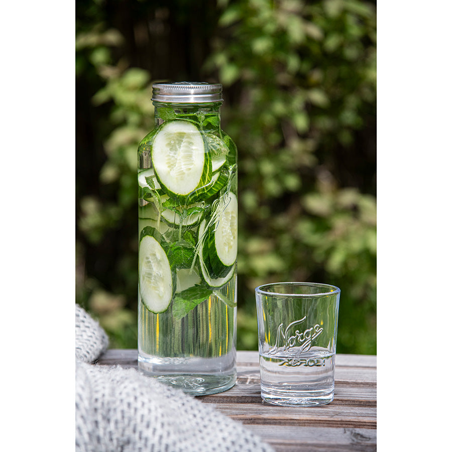 En Norgesglasset flaske fylt med agurk og mynte, plassert på et tredekk med en glass foran, ideell for å servere forfriskende drikke.