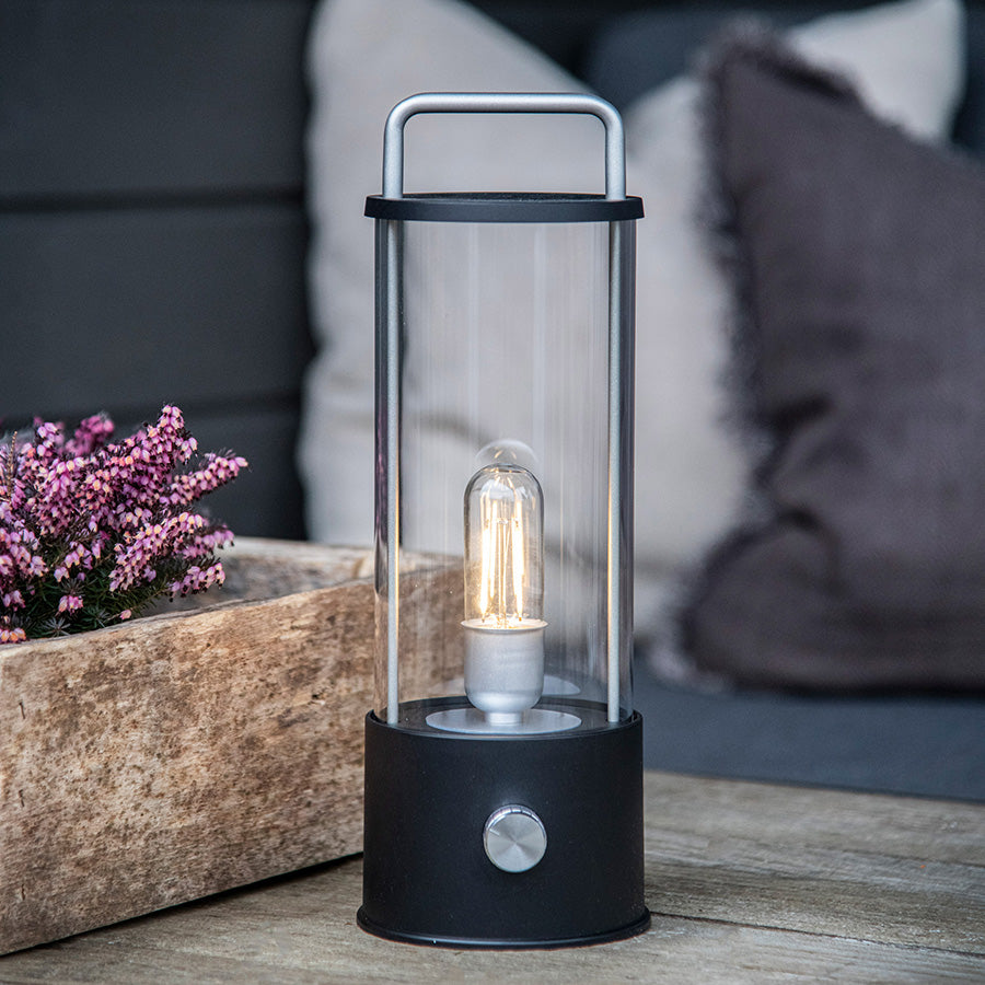 Norgesglasset Ledlampe i en hage setting ved siden av en blomsterkasse, skaper en avslappende atmosfære i kveldsbelysning.