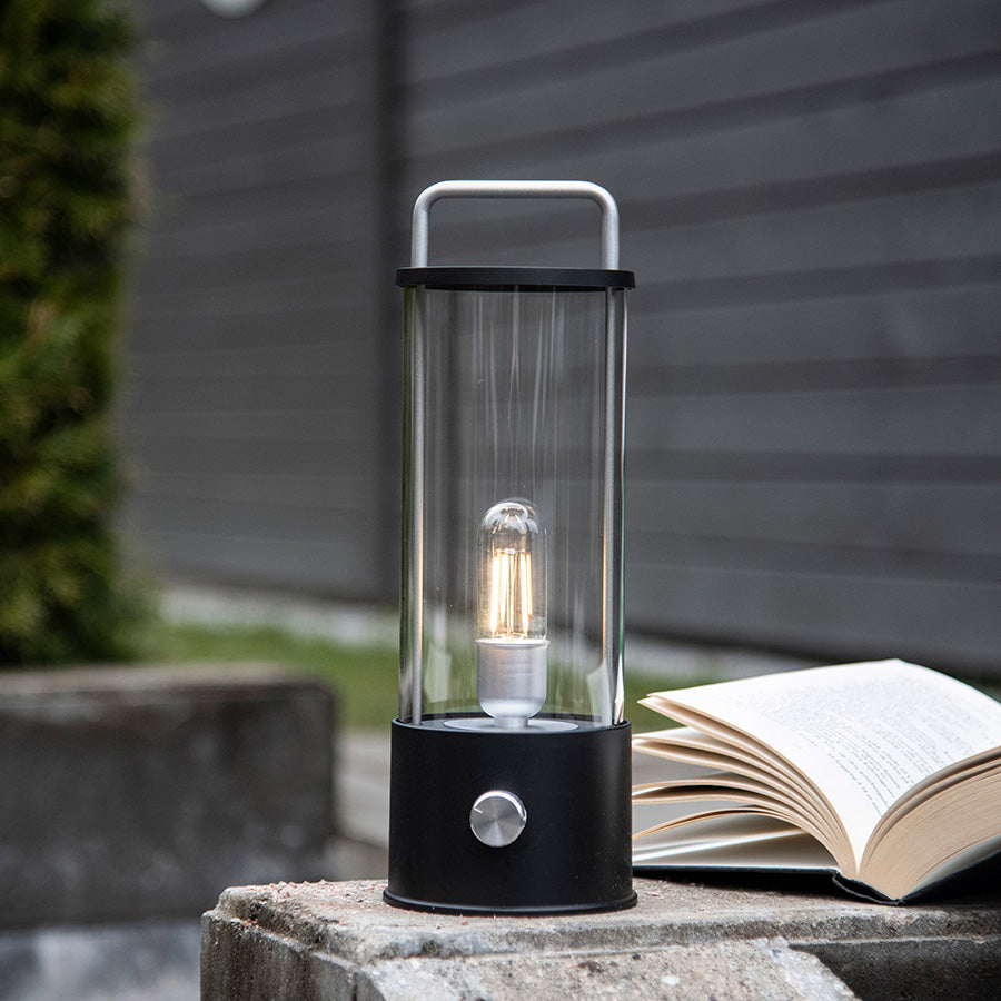 Norgesglasset Ledlampe plassert på en uteplass med en åpen bok ved siden av, gir perfekt lys for lesing i et utendørs miljø.