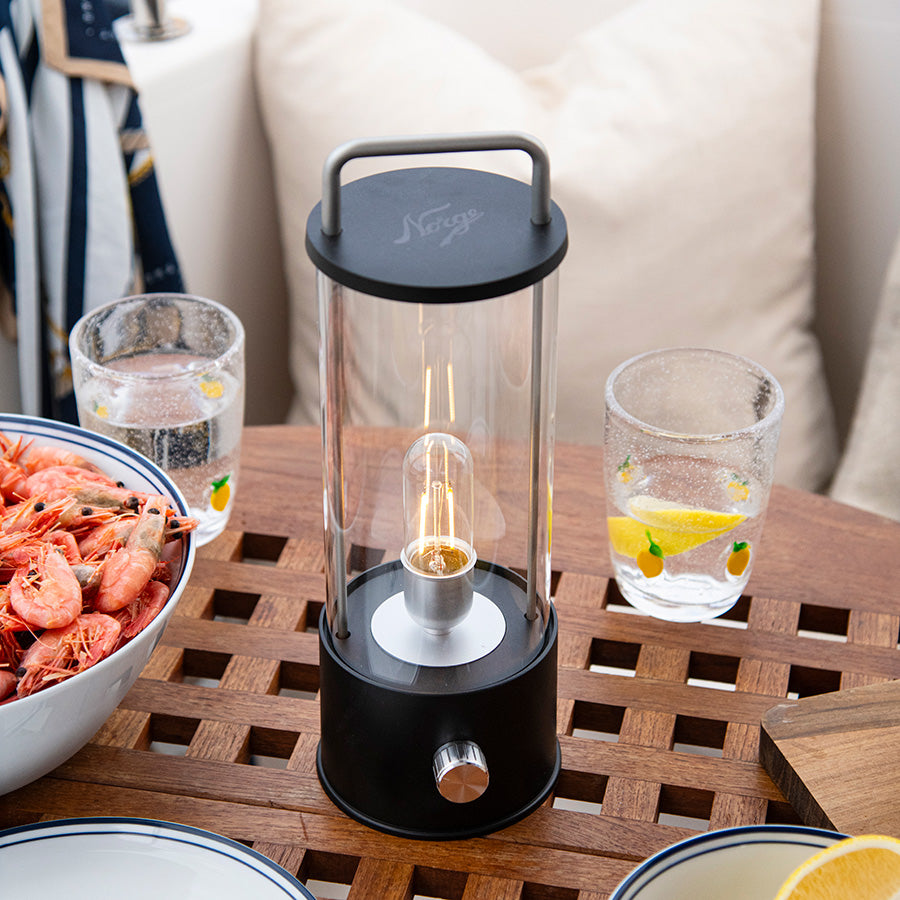 Norgesglasset Ledlampe med dimmer plassert på et bord med sjømat og drikke, gir et koselig lys for en hyggelig middag.