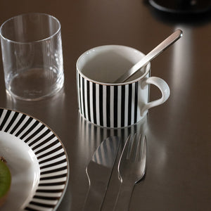 Klassisk Novak Abby krus med svart-hvitt stripemønster, plassert på et bord med bestikk og et glass ved siden av.