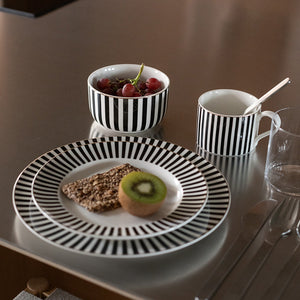 To Novak Abby krus i svart-hvitt stripemønster sammen med tallerkener og en bolle, perfekt for frokostbordet.