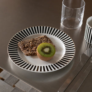 Nova Abby tallerken med svart-hvitt stripemønster og gullkant, servert med en brun kake og en skive kiwi på et bord.