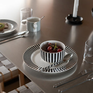 Elegant Nova Abby tallerken i svart og hvitt, ved siden av en bolle med druer, på et moderne dekket bord.