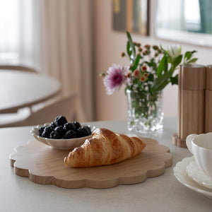 Rund skjærefjøl fra NOVA med et varmt preg, med croissant og bær på, perfekt for servering og skjæring.