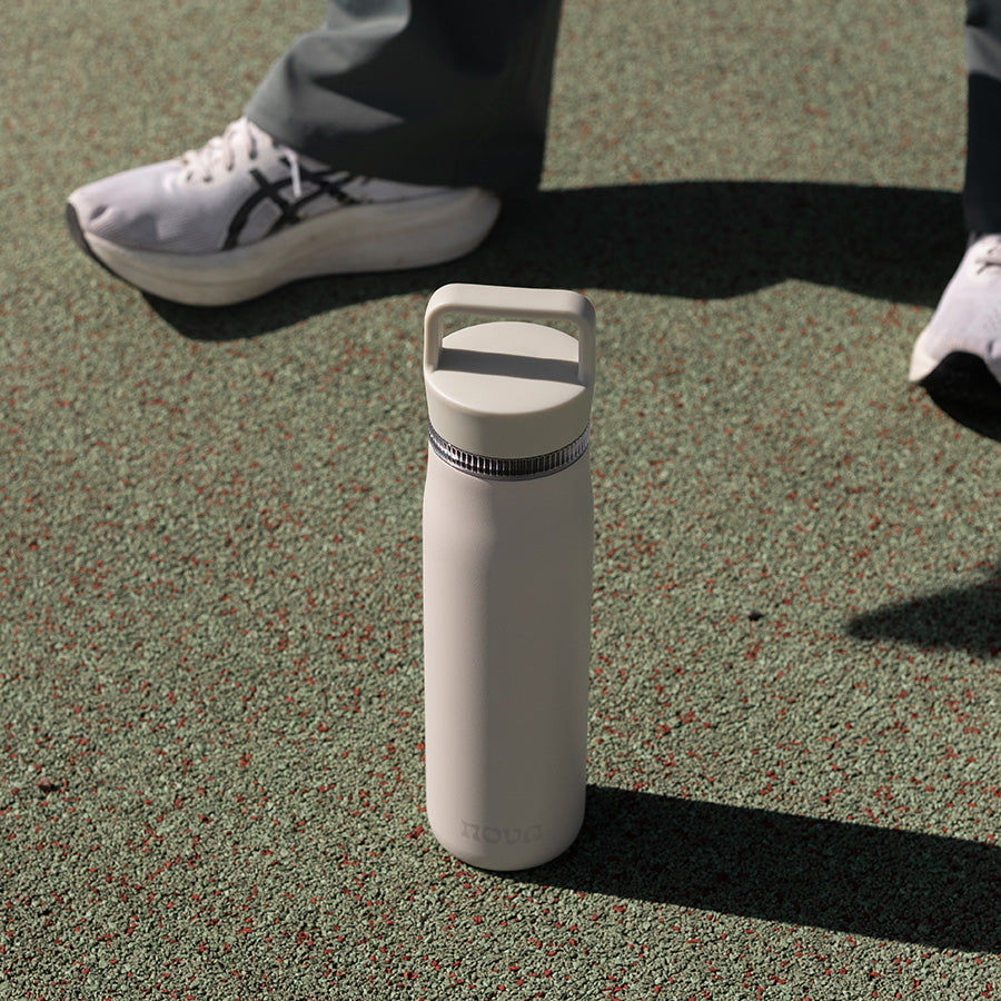 Drikkeflaske fra Nova Dynamic plassert på bakken med sneakers, perfekt til trening.