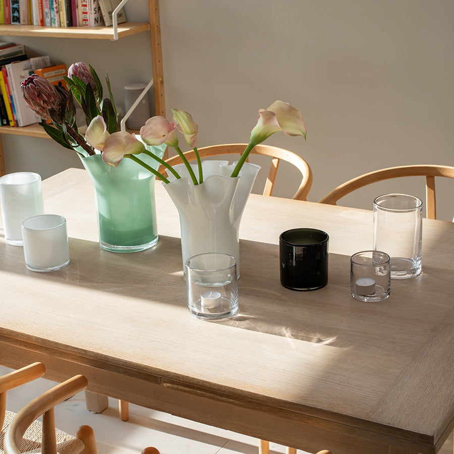 Klare lyslykter i glass på spisebord sammen med blomster og vaser i et lyst, nordisk interiør