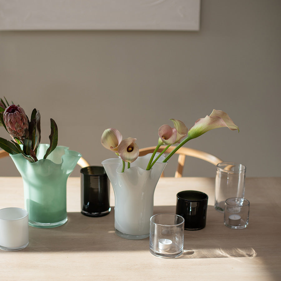 Transparente lyslykter i glass med levende lys på spisebord, dekorert med blomster og vaser