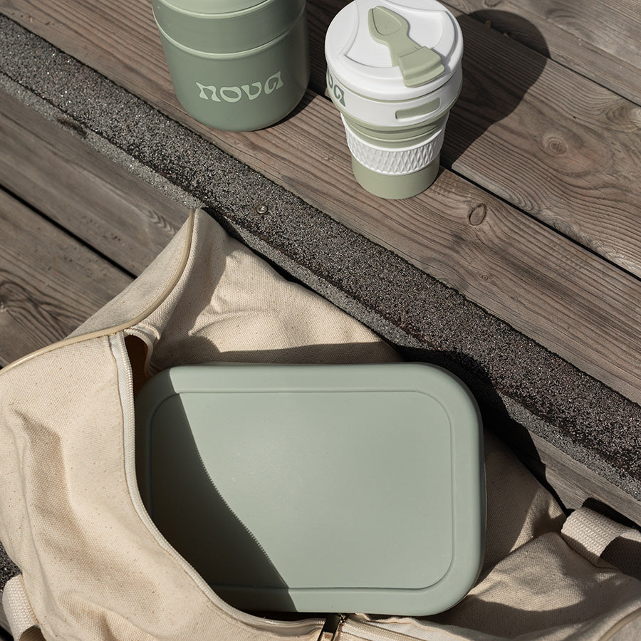 Grønn matboks plassert i en ergonomisk veske, sammen med en drikkekopp, ideelt for piknik eller tur.