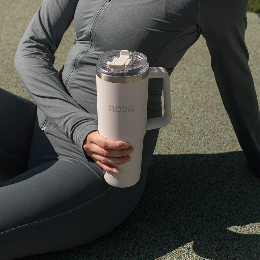Kvinne som holder termokopp i creme mens hun sitter, perfekt for kaffe eller te mens man er på farten.