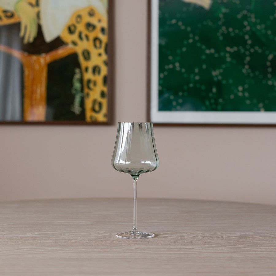 Elegant grønt stettglass på et bord, med en moderne stil og rillene som gir et behagelig grep, perfekt for servering av vin.