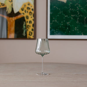 Elegant grønt stettglass på et bord, med en moderne stil og rillene som gir et behagelig grep, perfekt for servering av vin.