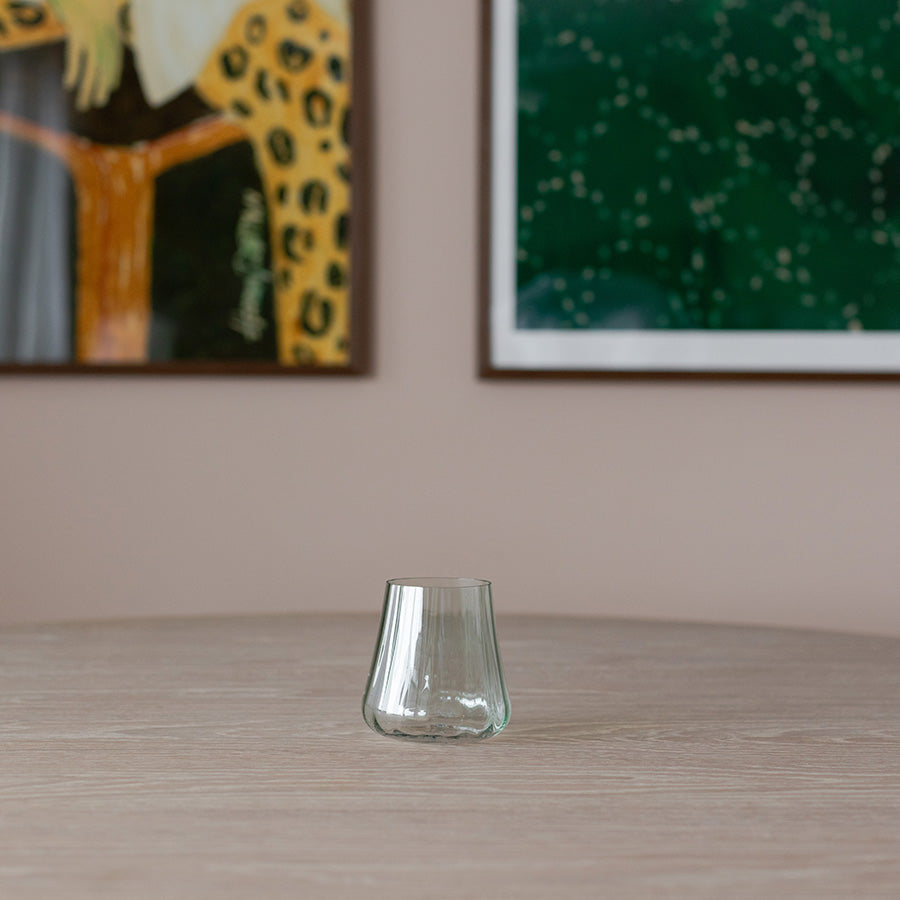 Nærbilde av et enkelt Nova Lottie vannglass i grønt plassert på et bord, med kunstverk i bakgrunnen som gir en stilren atmosfære.