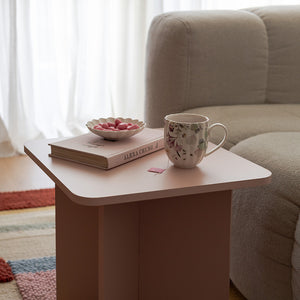 En koselig stuescene med Nova Lilly Krus 32cl Flower plassert på et rosa sidebord. Kruset, med delikat blomstermønster, gir et mykt og vårinspirert uttrykk, sammen med bøker og småretter, perfekt for en avslappende kaffepause.