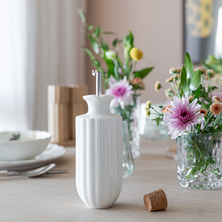 Nova Lilly Olje Dispenser 300ml Hvit i elegant design med blomsterinspirert form, perfekt for oppbevaring av olivenolje og dressinger, plassert på et bord med blomsterdekorasjoner.