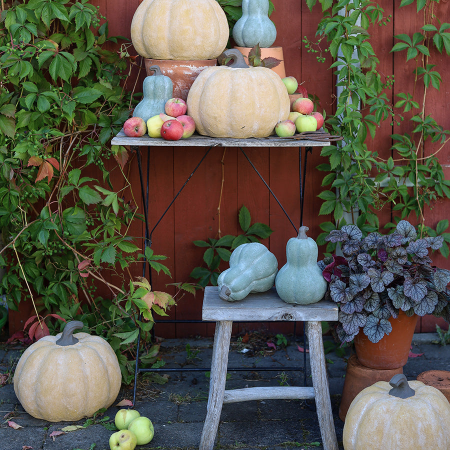 Grønne keramikkgresskar og oransje gresskar i høstdekorasjon med epler og planter