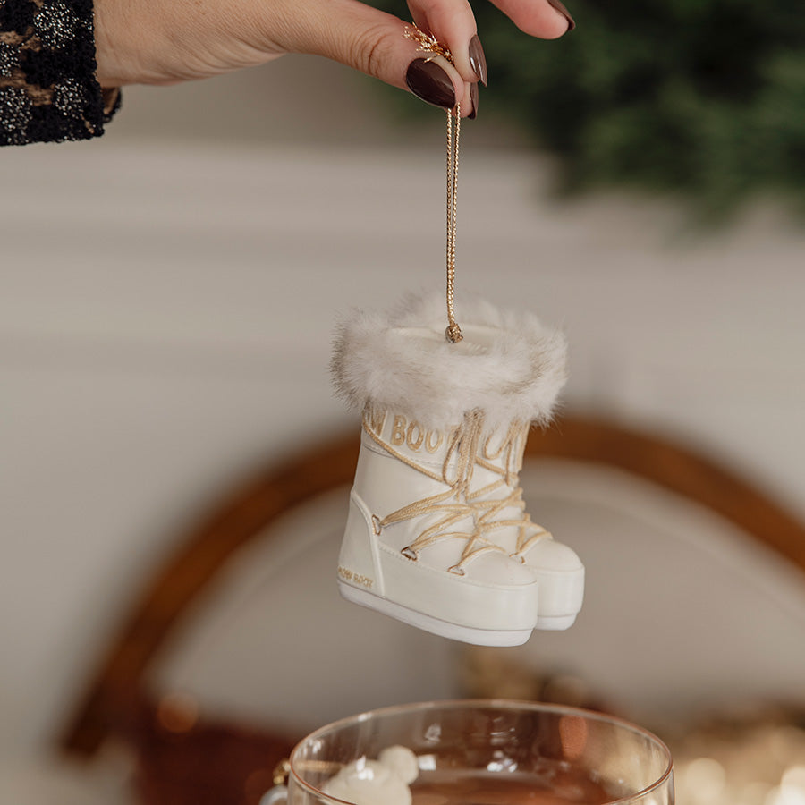 Hånd som henger opp et afterski-ornament med hvite snøstøvler og gulldetaljer