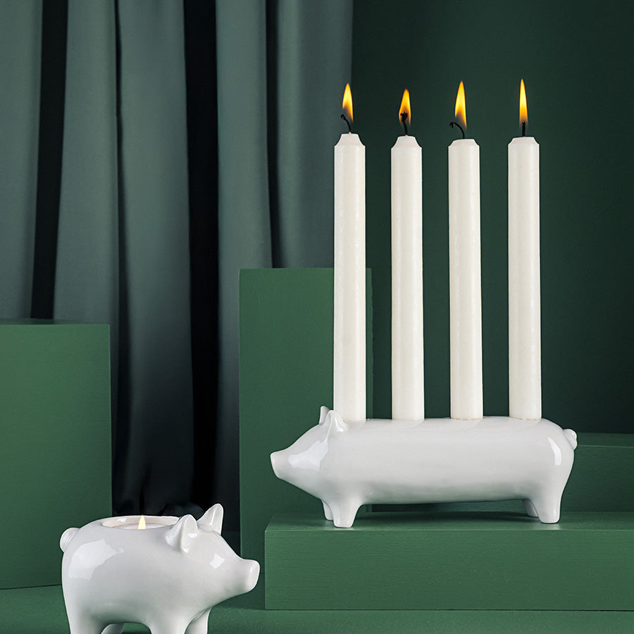 Hvit porselen adventstake formet som en heldiggris med fire tente lys, vist sammen med en liten griselysholder