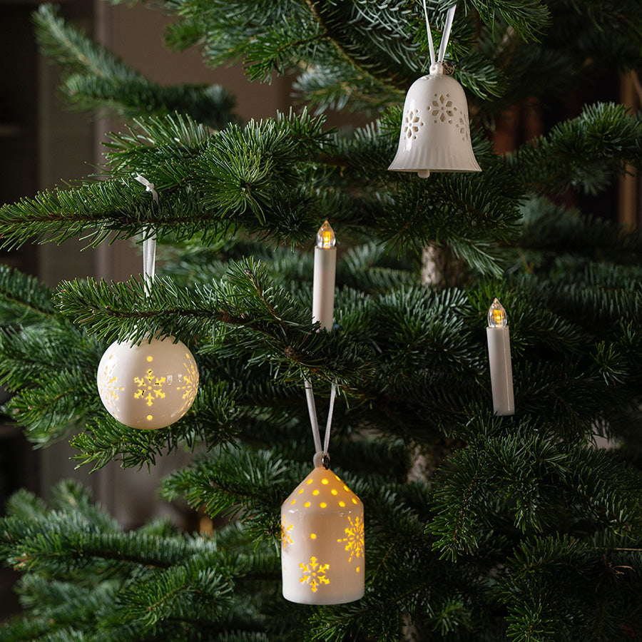 Hvite porselenshus som lysende ornament med LED-lys hengt på juletre sammen med annen julepynt