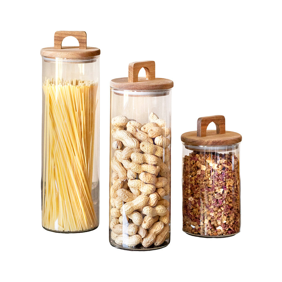 Tre oppbevaringsglass i forskjellig høyde med akasietrelokk, fylt med spaghetti, nøtter og tørkede blomster. Ideelle oppbevaringsglass for kjøkkenbenken.