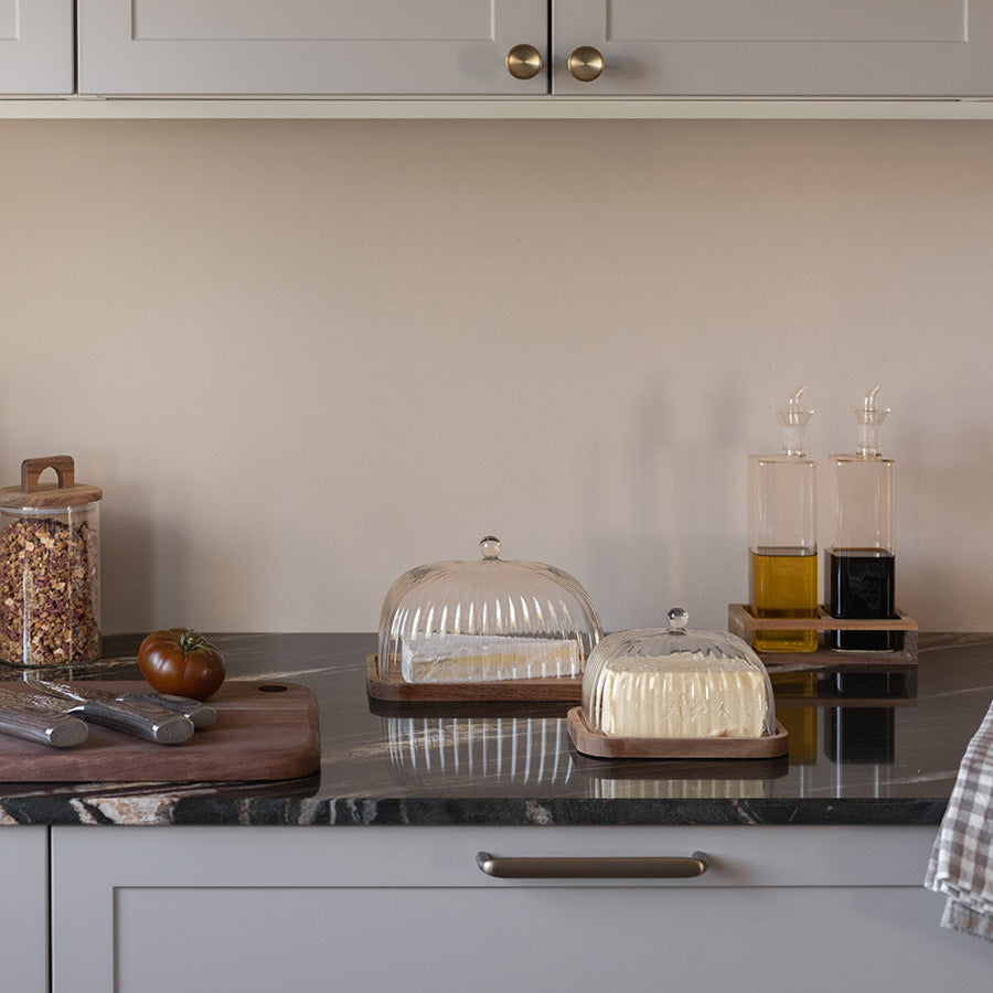 To smørklokker i ribbet glass fra Christiania 1739 Pantry-serien på kjøkkenbenken, som gir en stilfull presentasjon av smør.