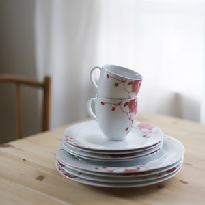 Porsgrund Porselænsfabrik Maxistrå Krus 35cl Nomi Rosa stablet sammen med tallerkener i Maxistrå-serien, på et bord med naturlig trebelegg.