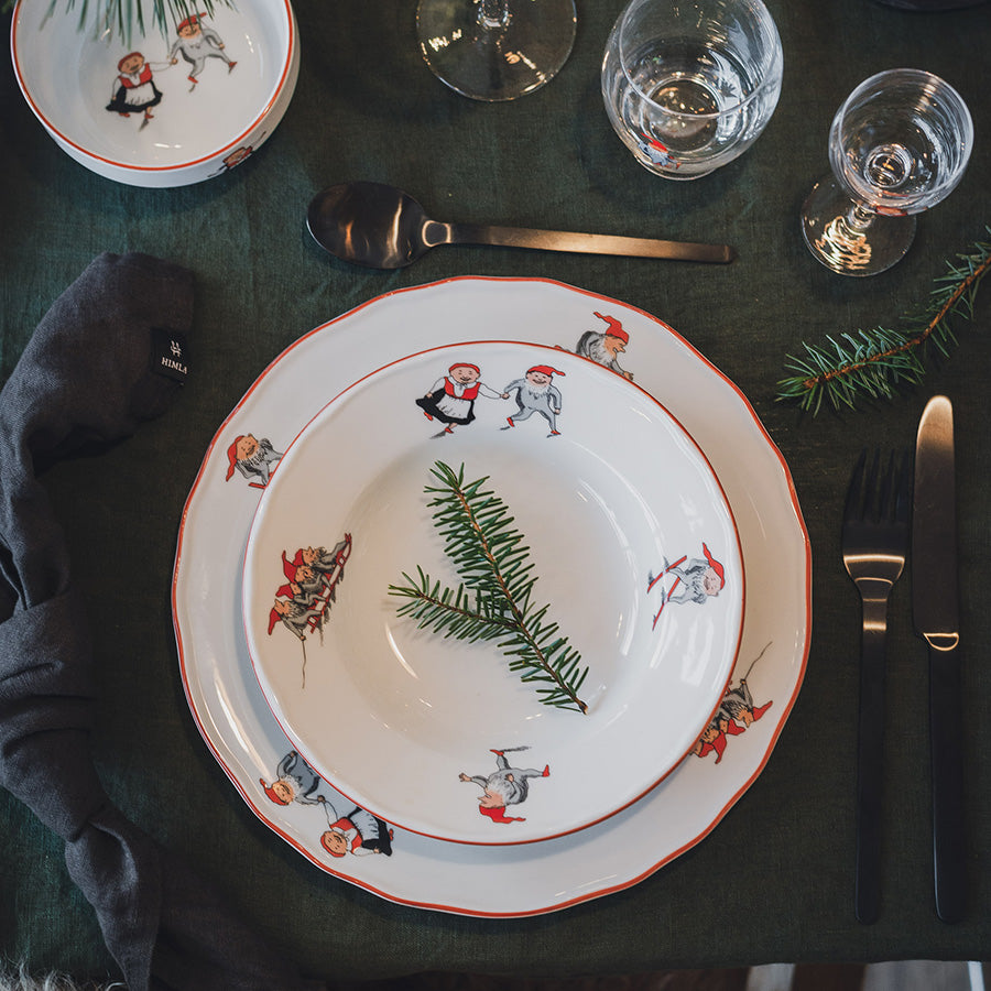 Dyp tallerken fra Nisseserviset dekket med julemiddag, med dekorerte tallerkener og glass. Ideell for å skape en stemningsfull juleopplevelse.