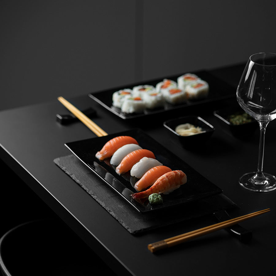Moderne sushi sett med elegant sort porselen, servert med nigiri, maki og tilbehør på et stilrent bord.