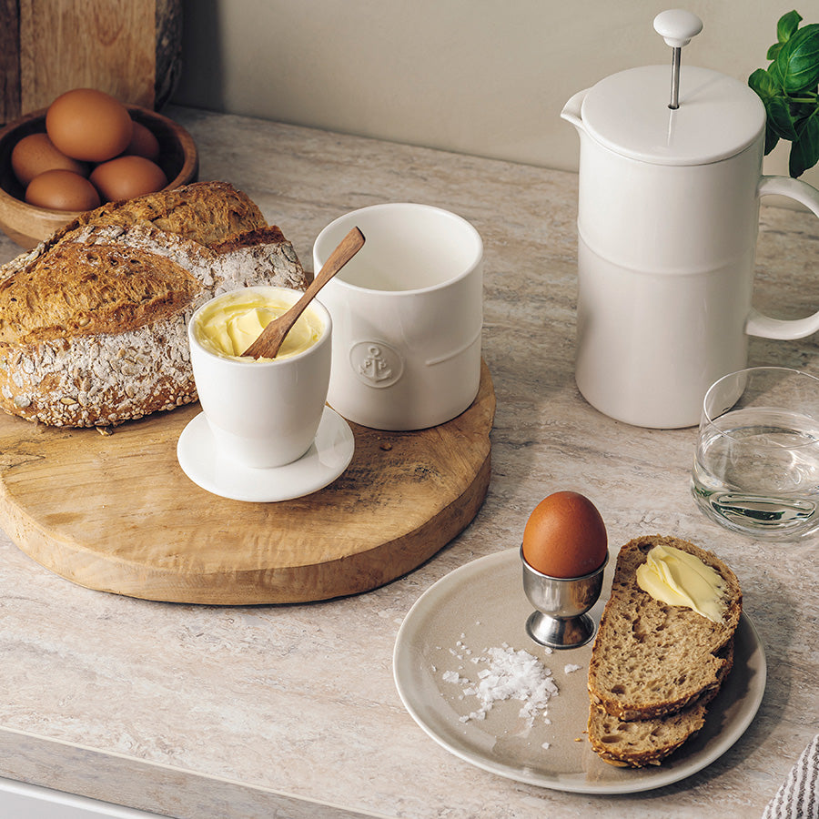 Porsgrund Porselænsfabrik Ildfast Smørklokke 10x12,4cm Hvit fylt med mykt smør, avbildet på frokostbordet sammen med brød og egg, viser hvordan smørklokken kombinerer funksjon og stil.