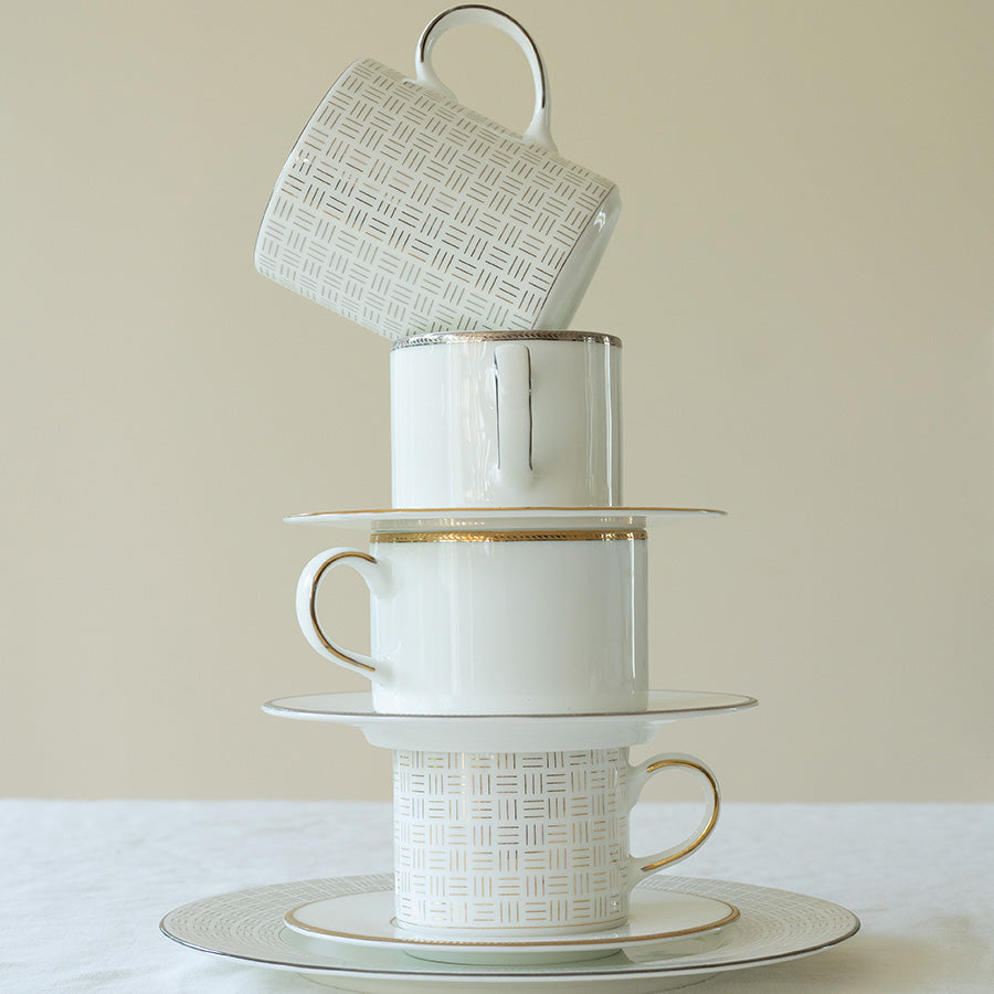 Porsgrunn Porselænsfabrik Vivienne Gull Krus 35cl stablet sammen med tallerkener og kopper, som viser eleganse og luksus i borddekking.