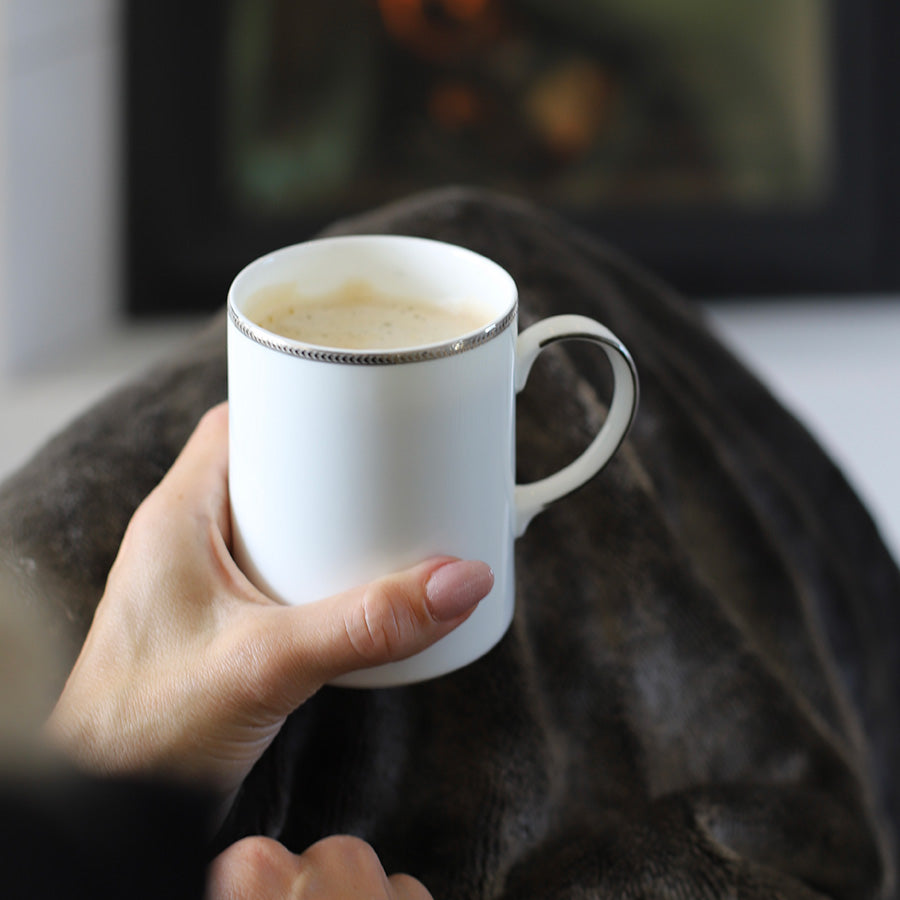 Håndholdt Porsgrund Porselænsfabrik Isabelle Platinum Krus 35cl fylt med varme drikker, plassert i en koselig setting med teppe, perfekt til hjemmet.