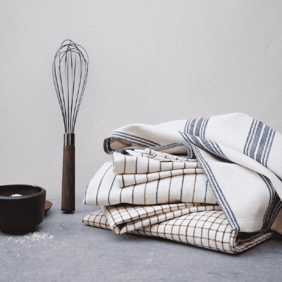 Stabel med flere Rosendahl kjøkkenhåndklær i forskjellige design, sammen med kjøkkenverktøy, perfekt for et stilrent kjøkken.