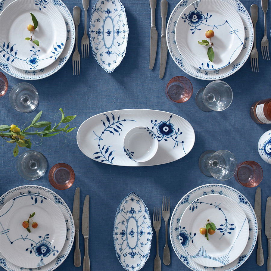 Royal Copenhagen Blå Mega Riflet ovalt serveringsfat 37 cm midt på et elegant dekket bord med andre serviser, perfekt for å vise fram mat på en stilfull måte.