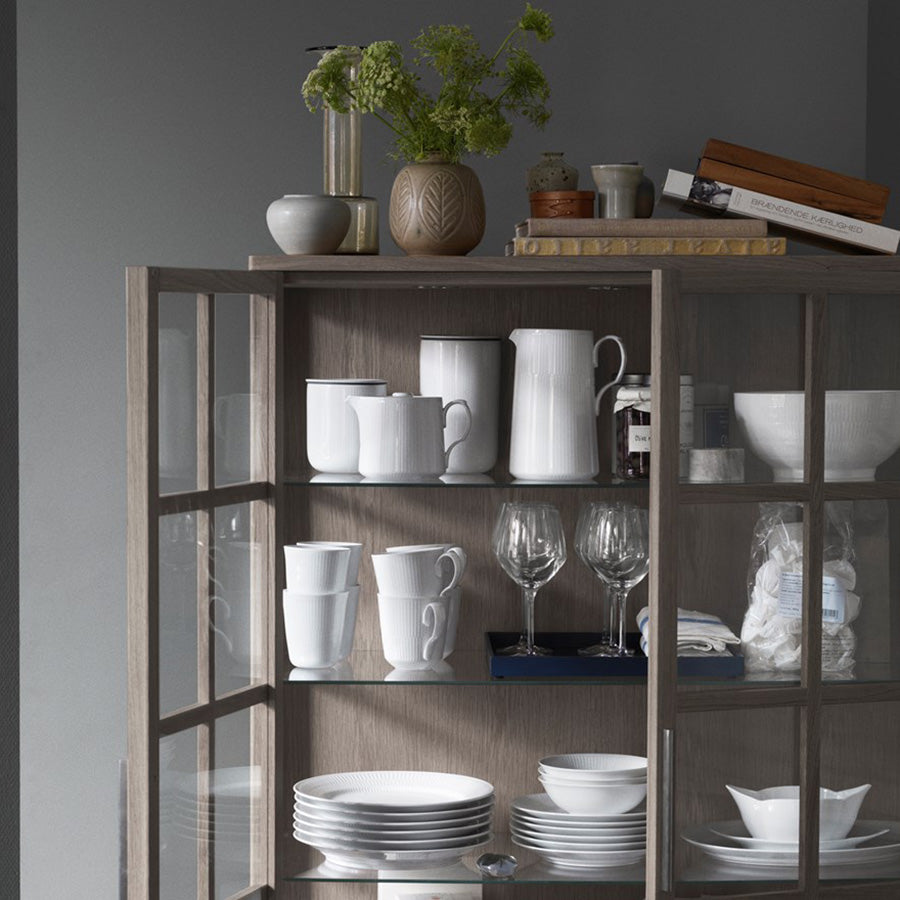Royal Copenhagen Hvit Riflet Skål 13 cm plassert i en stilfull hylle sammen med annet hvitt servise. Den skaper en harmonisk atmosfære i kjøkkeninnredningen.