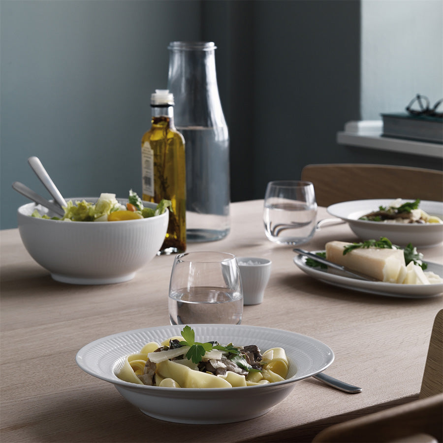 Royal Copenhagen Hvit Riflet Dyptallerken 21cm i en bordsetting med pasta og salat, fremhever den stilige bruken av dyptallerkenen.