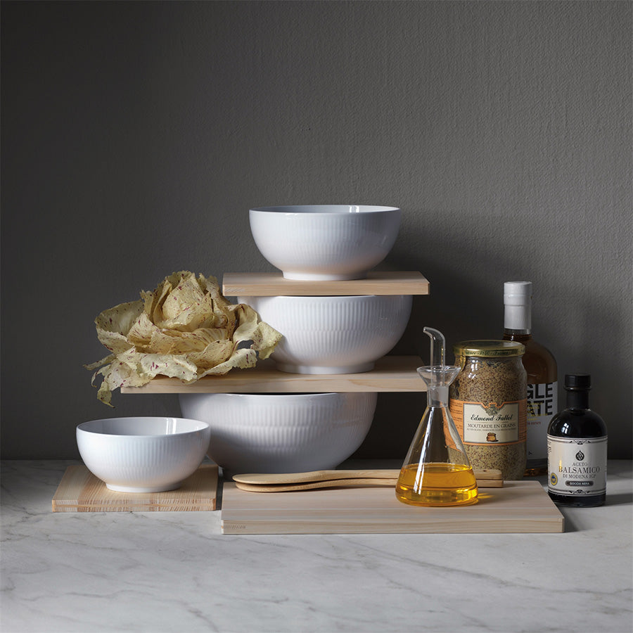 Royal Copenhagen Hvit Riflet Skål 18cm, stilfull samling av hvite skåler på treplater, ideelt for organisering av mat og ingredienser.